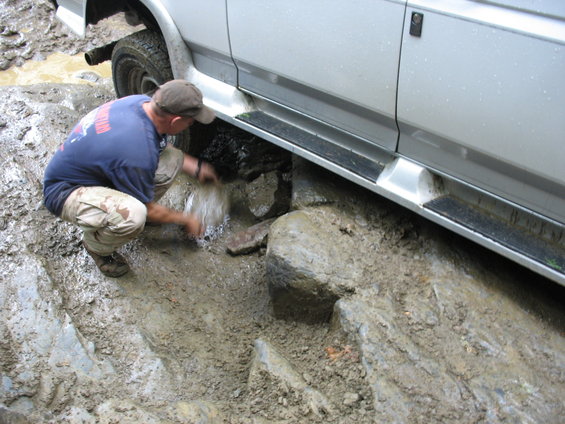 Silver van side with running boards stuck in mud, man cleaning undercarriage