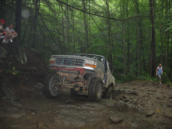 Silver Ford F-Series truck with lifted suspension navigating a rocky, muddy trail in a forest