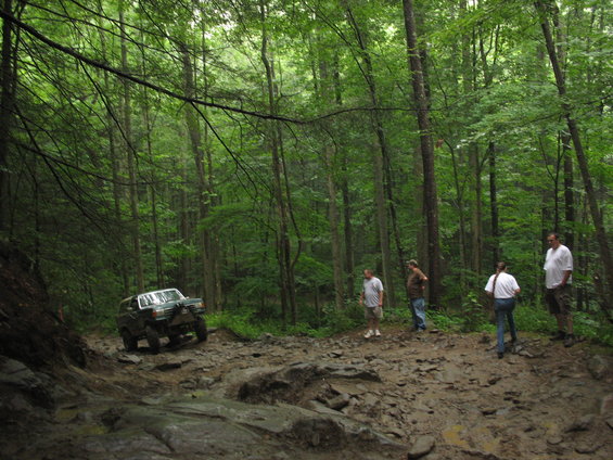 Off-road vehicle navigating a muddy, rocky trail in a dense forest