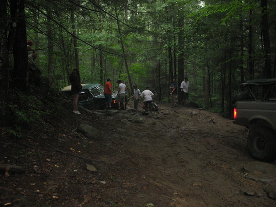 Off-road vehicles stuck in a muddy forest path with people observing