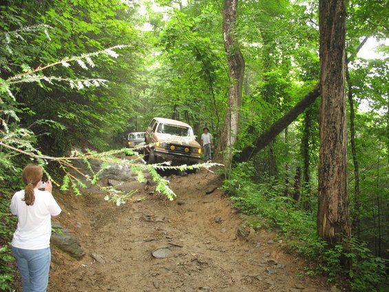 Tan SUV driving on a muddy trail with another vehicle behind it