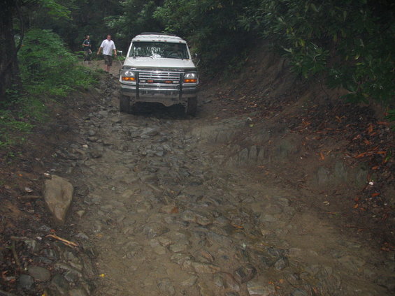 White Ford F-Series truck with aftermarket grille guard driving on a rocky, muddy trail