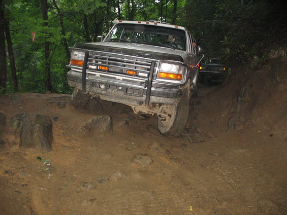 1995 Ford C-350 (Centurion Conversions) navigating a rocky, muddy trail with another vehicle behind it
