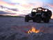 2002 Jeep Wrangler - A Jeep Wrangler sits on the beach near a campfire as the sun sets over the ocean.