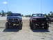 1994 Ford F-250 - Two modified Ford trucks are parked side-by-side on a sandy terrain under a clear blue sky.