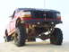 1994 Ford F-250 - A red Ford F-Series truck with a custom bumper and off-road tires is shown from a low front angle in a sandy environment.