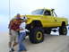 1994 Ford F-250 - A couple stands in front of a heavily modified yellow Jeep J-10 pickup truck on a sandy terrain.