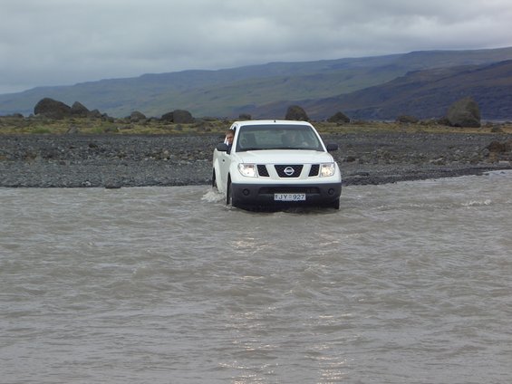 White Nissan pickup truck driving through a river, license plate JY-927