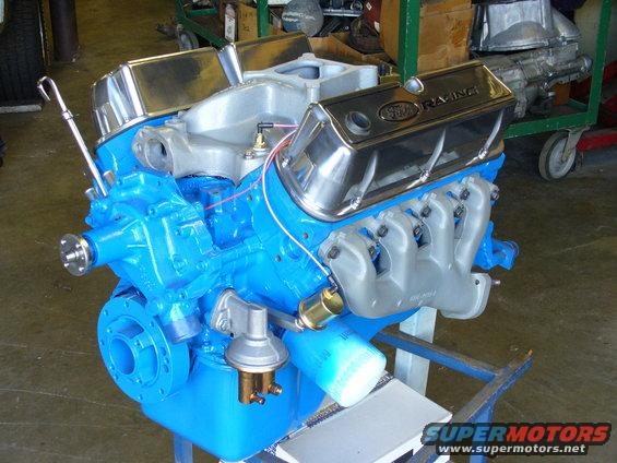 Blue Ford Racing engine with chrome valve covers and silver exhaust manifolds on a stand