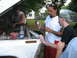 1990 Ford Bronco - Three men appear to be working on the engine of a white Ford Bronco, with tools and a beer bottle visible.
