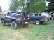 1990 Ford Bronco - Two modified pickup trucks are parked on a grassy lawn, with one having its hood open.