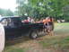 1990 Ford Bronco - A group of people are gathered around the bed of a black pickup truck in a grassy outdoor setting.