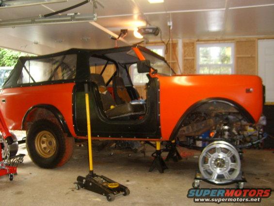 Orange International Harvester Scout II with soft top removed, doors off, and sitting on jack stands in a garage