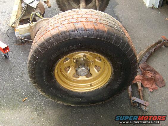 Close-up of a gold-colored wheel with a tire, next to leaf springs and other vehicle components