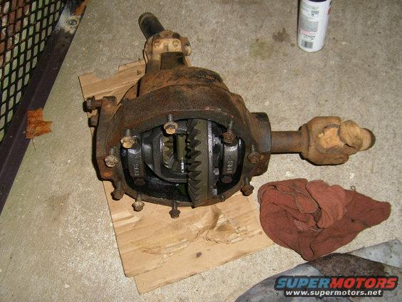 Rusty differential axle with open casing showing gears, resting on cardboard