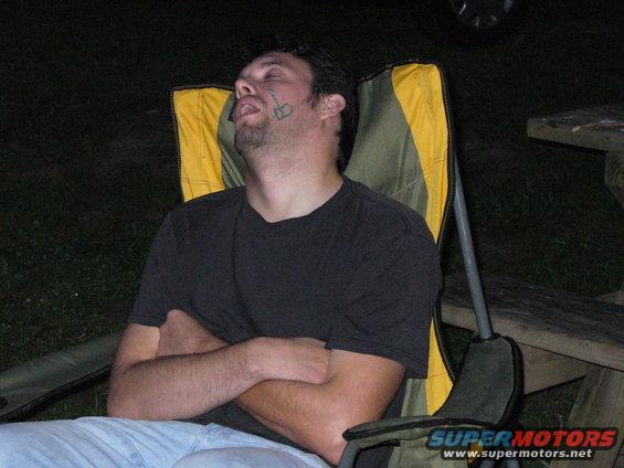 man sleeping in a camping chair with arms crossed, tattoo on his face