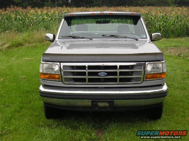Front view of a gray 1995 Ford F-150 truck parked on grass with a cornfield in the background