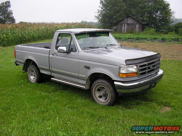 Gray Ford F-150 pickup truck parked in a grassy field with a cornfield and barn in the background