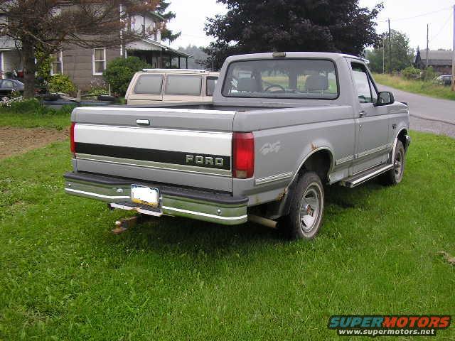 Gray Ford F-150 pickup truck, rear 3/4 view, parked on grass