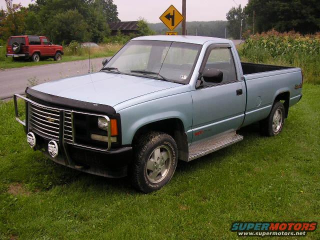 Light blue pickup truck parked on grass with a red SUV in the background