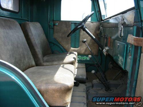 Interior view of an old green truck showing two bucket seats, a steering wheel, and gear shifters