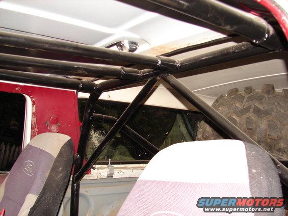 Interior view of a vehicle with a black roll cage, spare tire, and seats visible