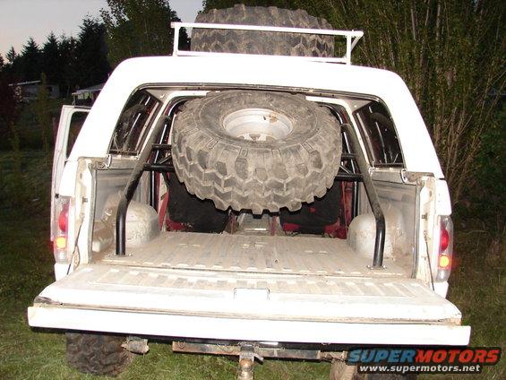 White 1996 Ford Bronco rear view, spare tire inside and on roof rack, aftermarket roll cage