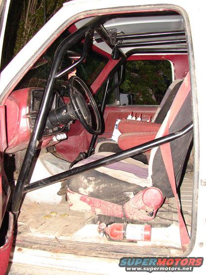 Interior view of a vehicle with a roll cage, racing seats, and a fire extinguisher