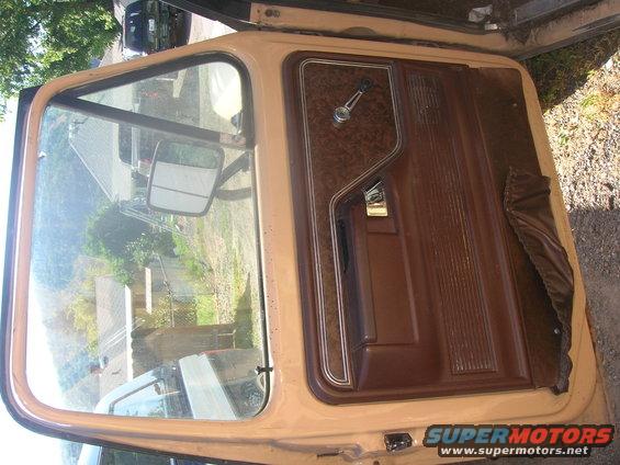 Interior door panel with woodgrain trim and crank window, reflection shows other vehicles outside