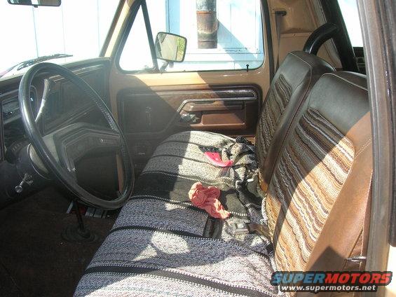 1978 Ford Bronco interior showing striped cloth seats, a blanket, steering wheel, and door panel
