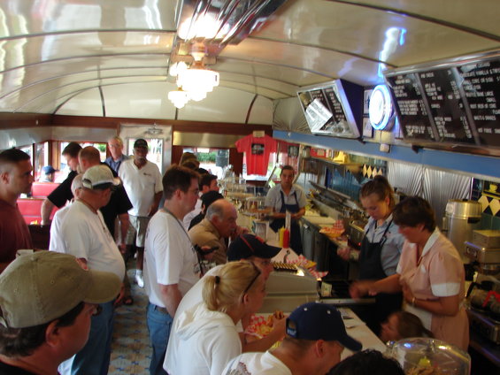 Interior of a diner with people at the counter and standing in line. Menu boards are visible
