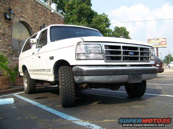 White Ford Bronco parked in a lot, front 3/4 view. Visible grille, headlights, and tires