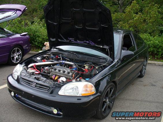 Black coupe with hood open, showing engine and front bumper details. A purple car is visible to the left