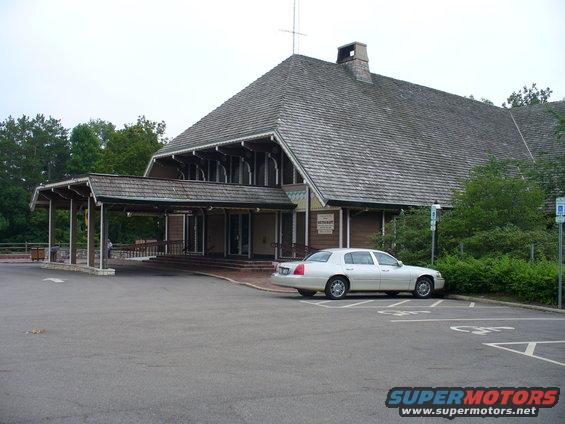 White sedan parked in a lot in front of a large building with a covered entrance