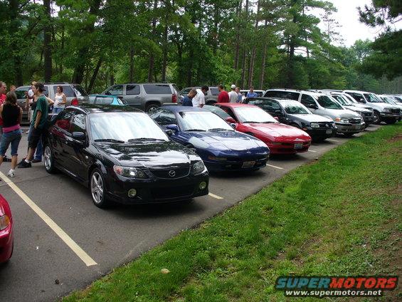 Several cars parked in a lot with trees in the background