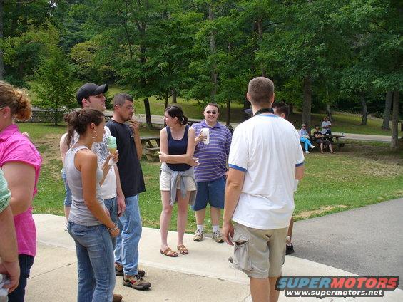 People gathered in a park setting with trees and picnic tables