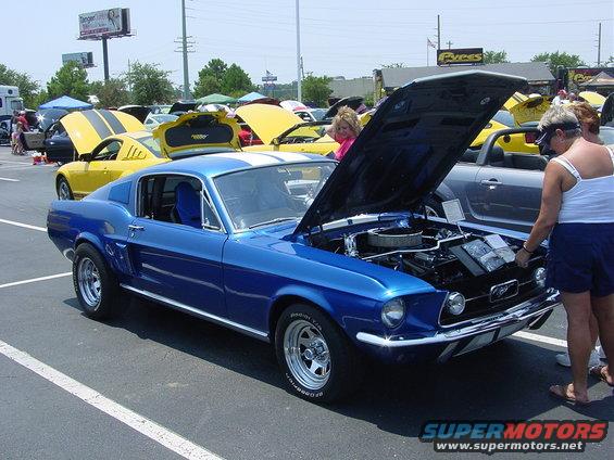 Blue 1967 Ford Mustang coupe with hood open, white stripes, parked at car show