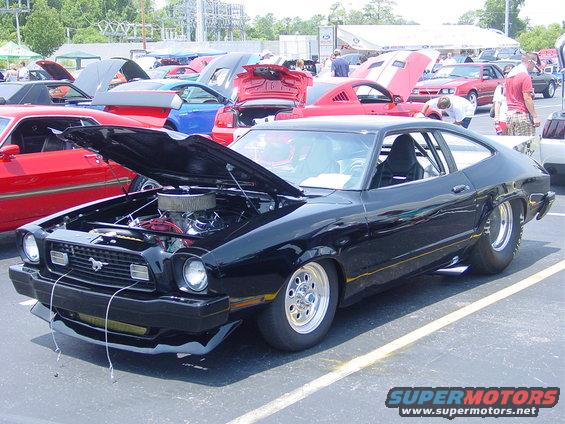 black coupe with hood open, showing engine, parked at car show