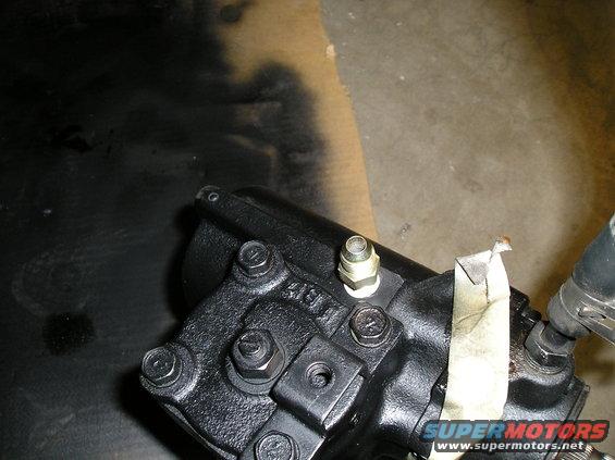 Close-up of a black steering gear box with bolts and a brass fitting