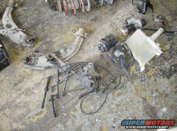 Assorted car parts including suspension components and spark plug wires on a concrete floor