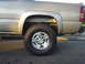 2002 Chevrolet Silverado 2500 - The rear wheel and fender of a gold Chevrolet Silverado 2500 pickup truck are visible in this side view.