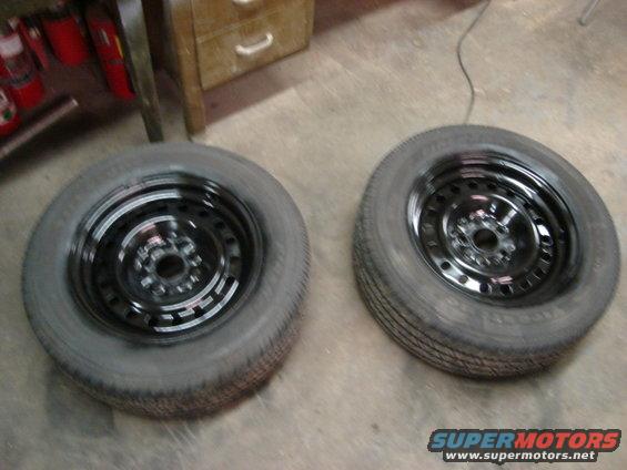 Two black steel wheels with tires on a concrete floor