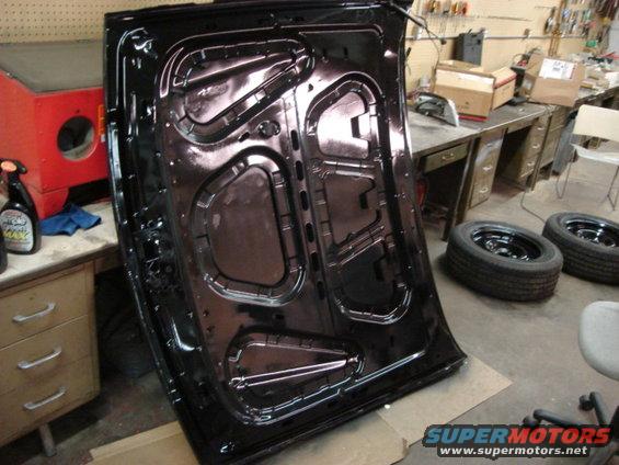 Black car hood interior in a workshop with tools and tires in the background