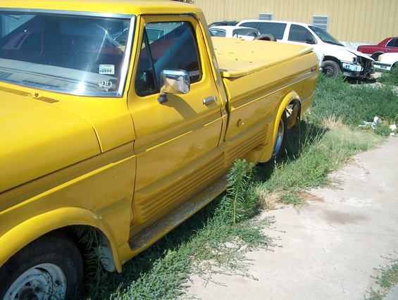 yellow pickup truck parked next to grass, with other vehicles in background
