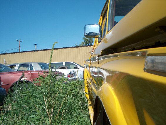 Close-up of yellow vehicle fender and side mirror. Other cars visible in background