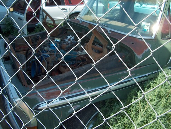 Green 1978 Ford Bronco with open hood, showing engine, behind a chain-link fence
