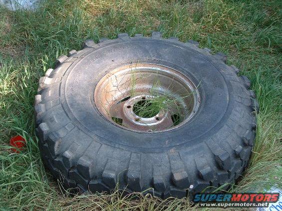 old off-road tire on a rusty rim sitting in the grass