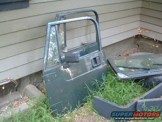 Green Jeep YJ door leaning against a wall, with a windshield frame and other parts on the ground