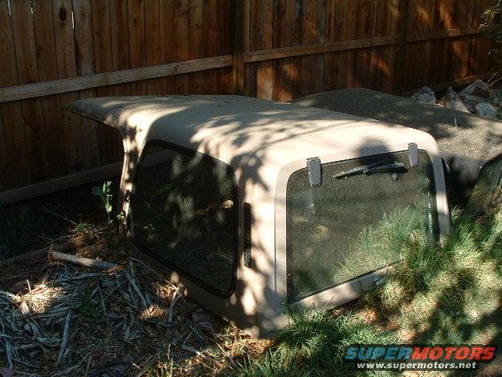 Jeep hardtop sitting on the ground near a wooden fence