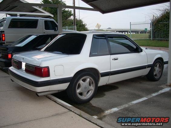 White 1991 Ford Mustang coupe parked under a carport, rear-wheel drive, with a black car behind it